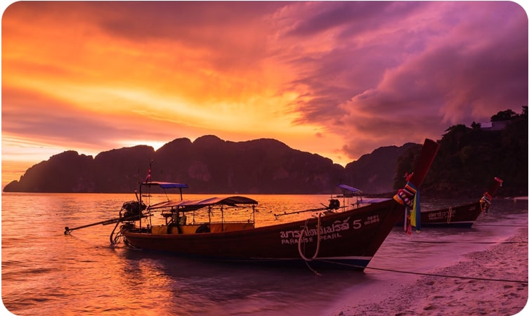 A stunning sunset over the water with traditional longtail boats at Koh Phi Phi, a must-visit place in Thailand for its stunning scenery