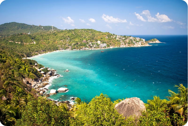 A stunning panoramic view of Shark Bay on Koh Phangan, Thailand, with its crescent-shaped beach, crystal-clear turquoise waters, and lush green hills.